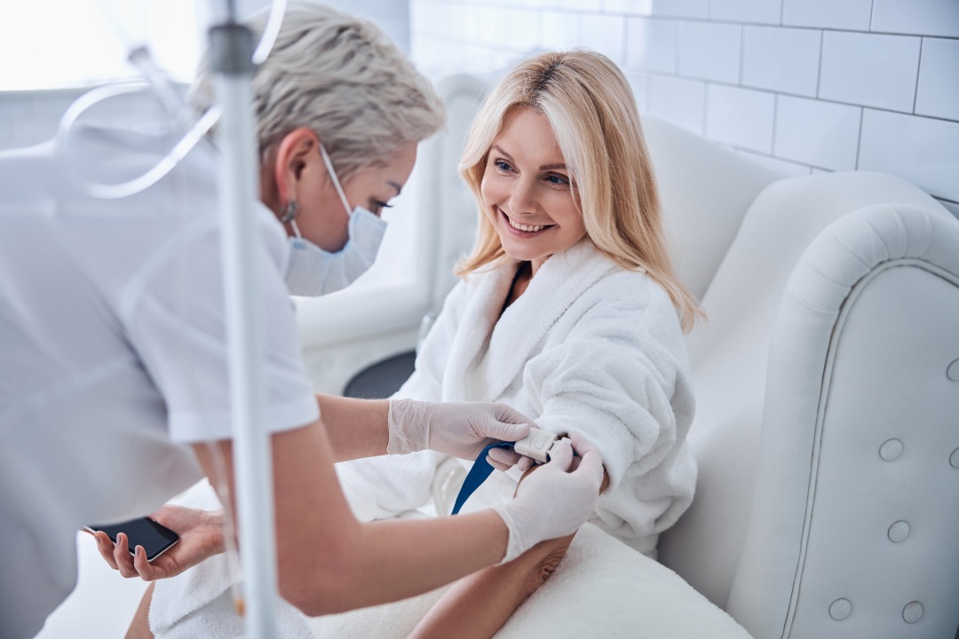 Side view portrait of happy cheerful talking with professional doctor while receiving IV infusion in beauty clinic